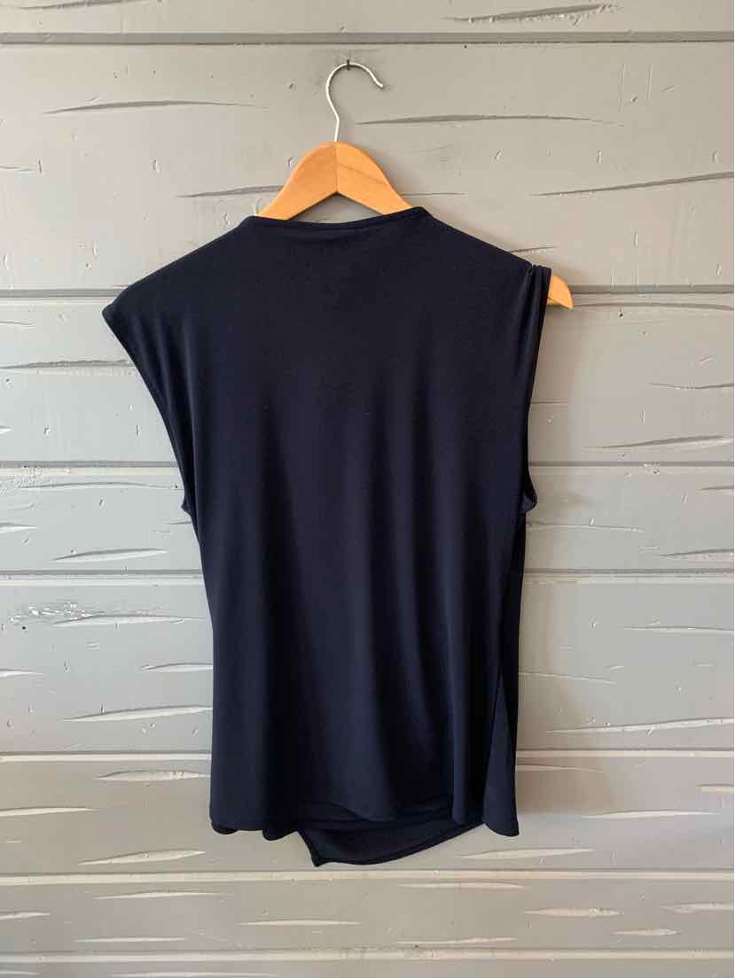 Black sleeveless knit top with mock neck hanging on wooden hanger against gray textured wall.