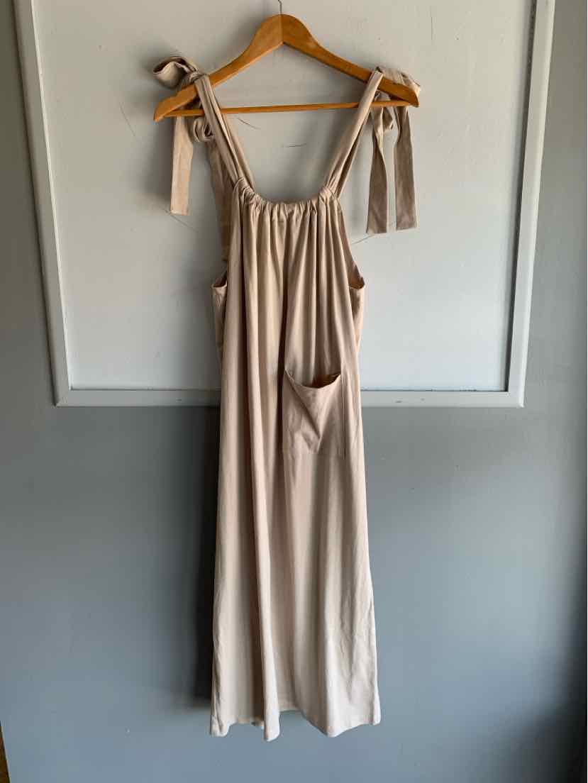 Beige sleeveless jumpsuit with adjustable tie straps and a front pocket, loose fit, gathered neckline.