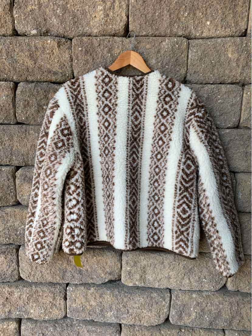 White and brown striped knit sweater with geometric patterns and long sleeves, hanging on wooden hanger.