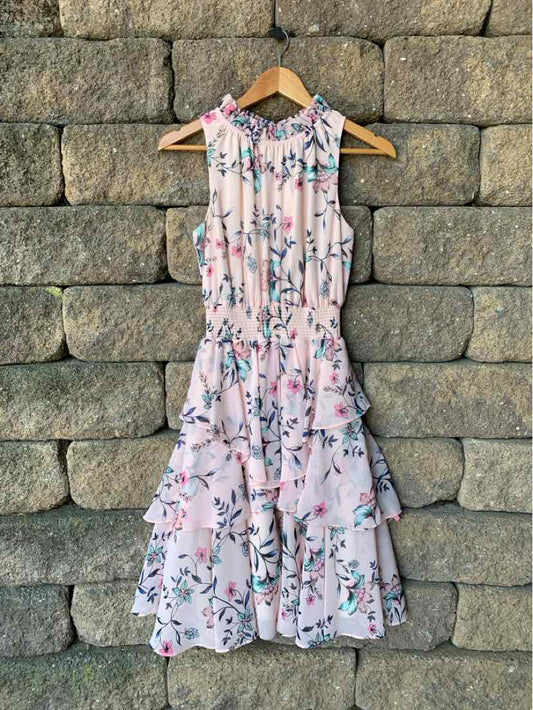 Sleeveless pink floral dress with ruffled skirt and cinched waist, knee-length design.