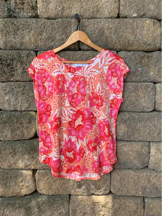 Pink floral short-sleeve blouse with round neckline and relaxed fit hanging on wooden hanger.