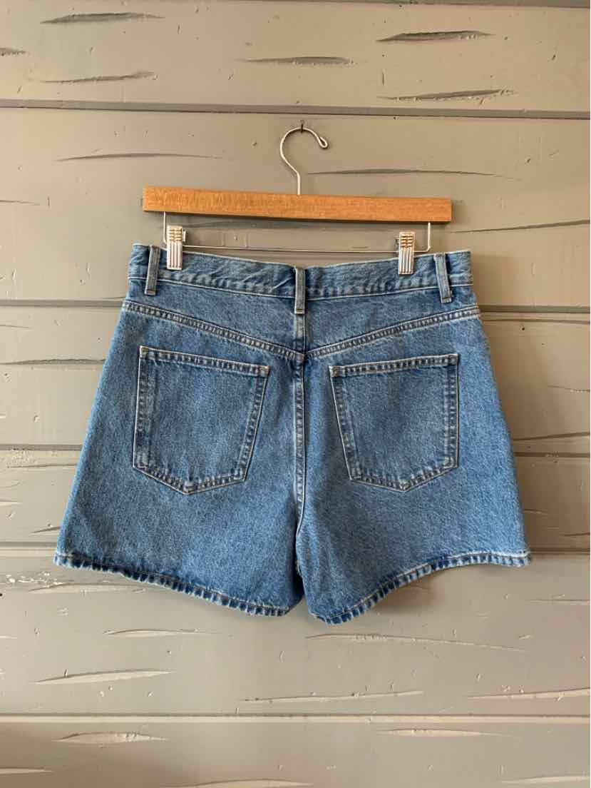 High-waisted blue denim shorts with back pockets and belt loops on a wooden hanger.