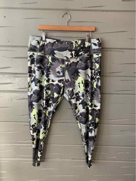 Multi-color abstract print leggings with high waistband in size 2X hanging on wooden hanger against gray wooden wall.
