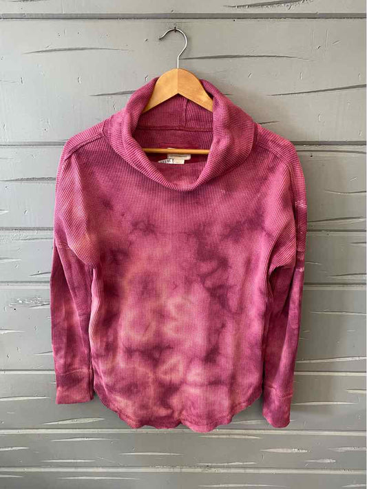 Pink tie-dyed long-sleeve turtleneck sweater with relaxed fit on wooden hanger.