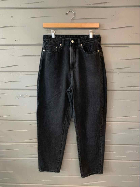 High-waisted black denim jeans with a tapered leg and five-pocket design hanging on wooden hanger.