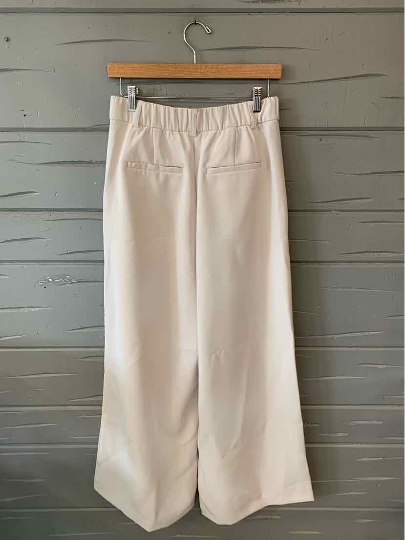 White wide-leg pants with elastic waistband and two rear welt pockets hanging on wooden hanger.