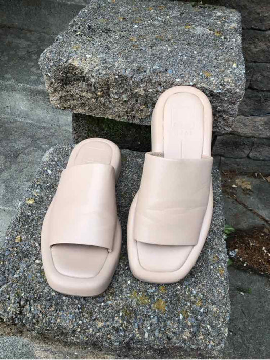 Nude slip-on sandals with wide strap and square toe on stone surface.