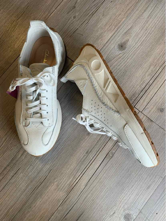 White leather women's Clarks sneakers with perforated sides and white laces on a wooden floor.