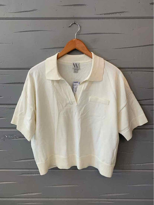White oversized casual top with short sleeves and collar hanging on wooden hanger against gray wall.