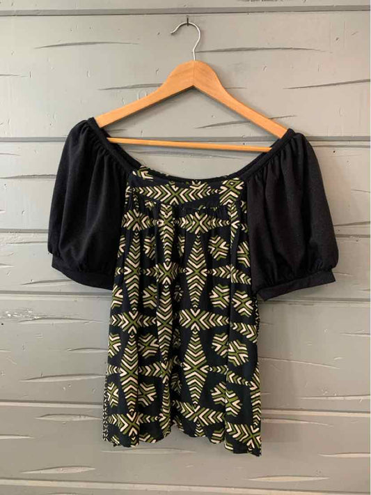 Black blouse with beige geometric patterns and puffed short sleeves hanging on wooden hanger.
