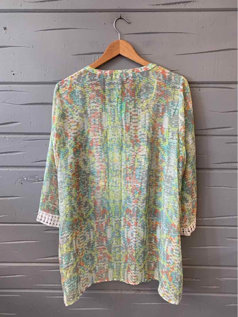 Long-sleeve tunic with green and pastel floral pattern in size 1X hanging on wooden hanger.