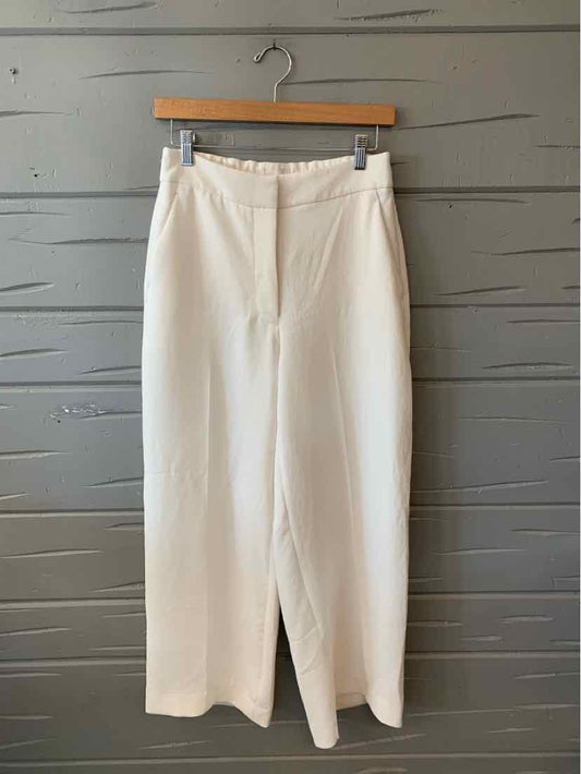 Cream high-waisted wide-leg trousers with front zipper and belt loops, hanging on wooden hanger.
