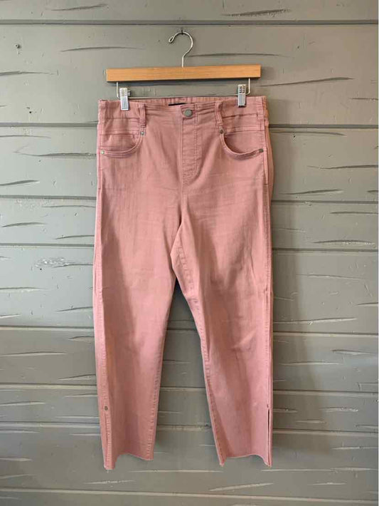 Light pink straight-leg pants with front pockets and belt loops hanging on wooden hanger against gray wood panel wall.
