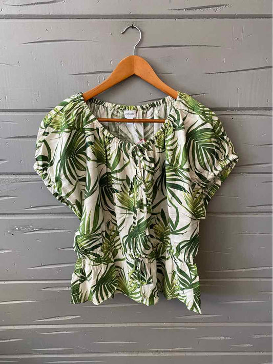 White blouse with green palm leaf print, puffed short sleeves, and ruched neckline on wooden hanger.