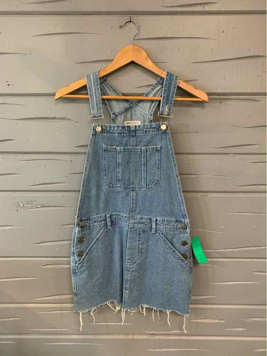 Blue denim overall dress with adjustable straps and frayed hem hanging on wooden hanger.