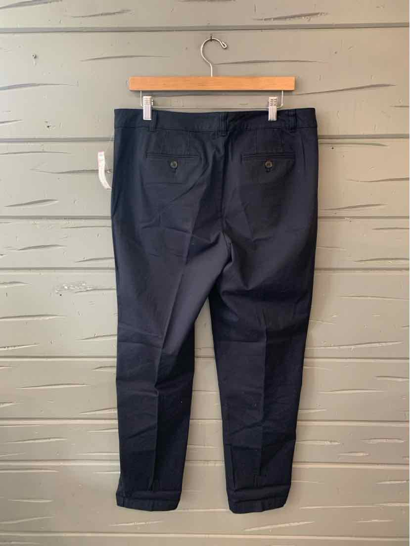 Black tailored pants with back buttoned pockets hanging on wooden hanger against light wood background.