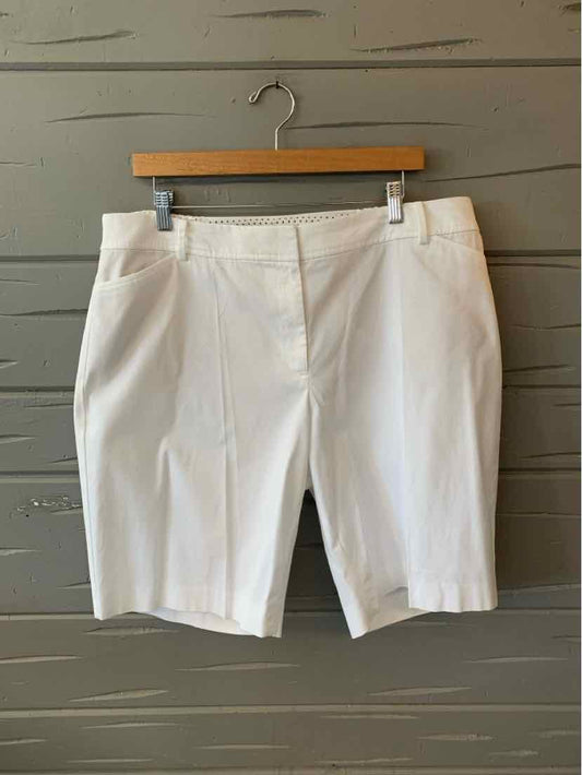 White tailored knee-length shorts with front pleats and side pockets, hanging on wooden hanger.
