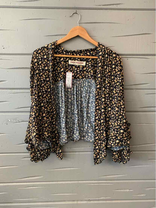 Black floral long-sleeve blouse with smocked waist and ruffled cuffs hanging on wooden hanger.