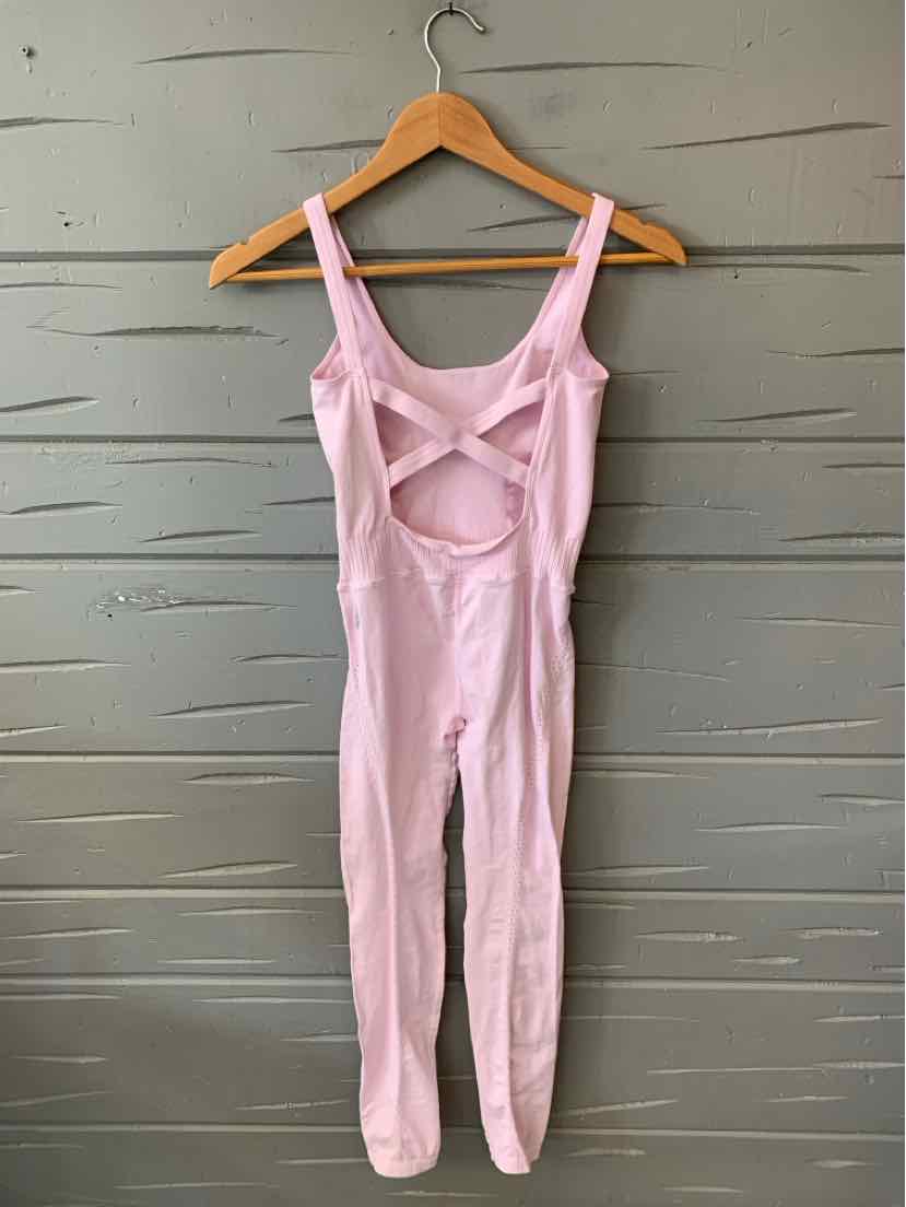 Light pink sleeveless jumpsuit with wide straps, cut-out front detail, and fitted legs in a soft fabric.