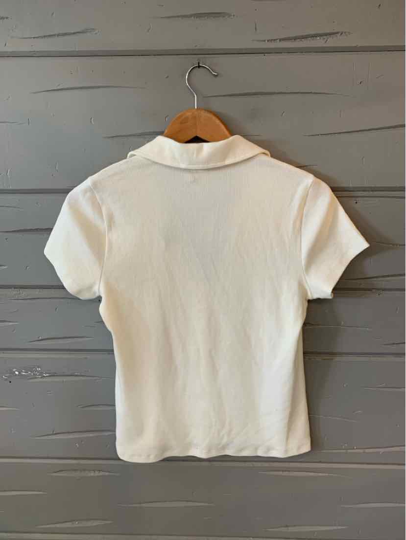 White short-sleeve polo shirt with collar, fitted cut, hanging on wooden hanger against gray wall.