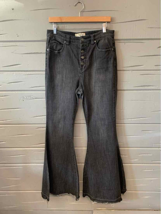 Black high-rise denim jeans with flared legs and a button fly closure hanging on wooden hanger.
