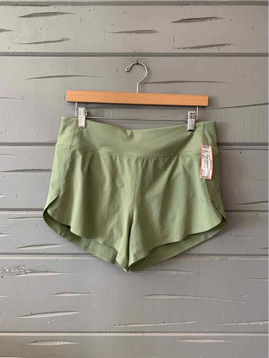 Light olive green athletic shorts with a smooth, lightweight fabric and curved hem hanging on a wooden hanger against a gray