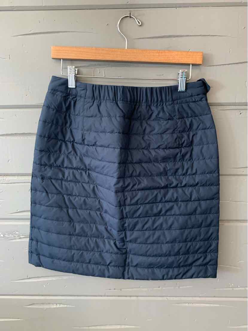 Black quilted skirt with horizontal stitching and elastic waistband hanging on wooden hanger.