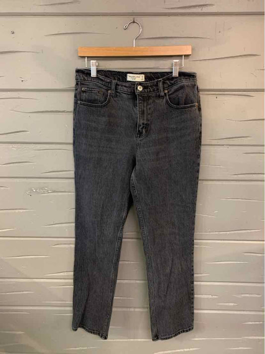 Black high-waisted straight-leg jeans with front pockets and belt loops hanging on wooden hanger against gray wall.