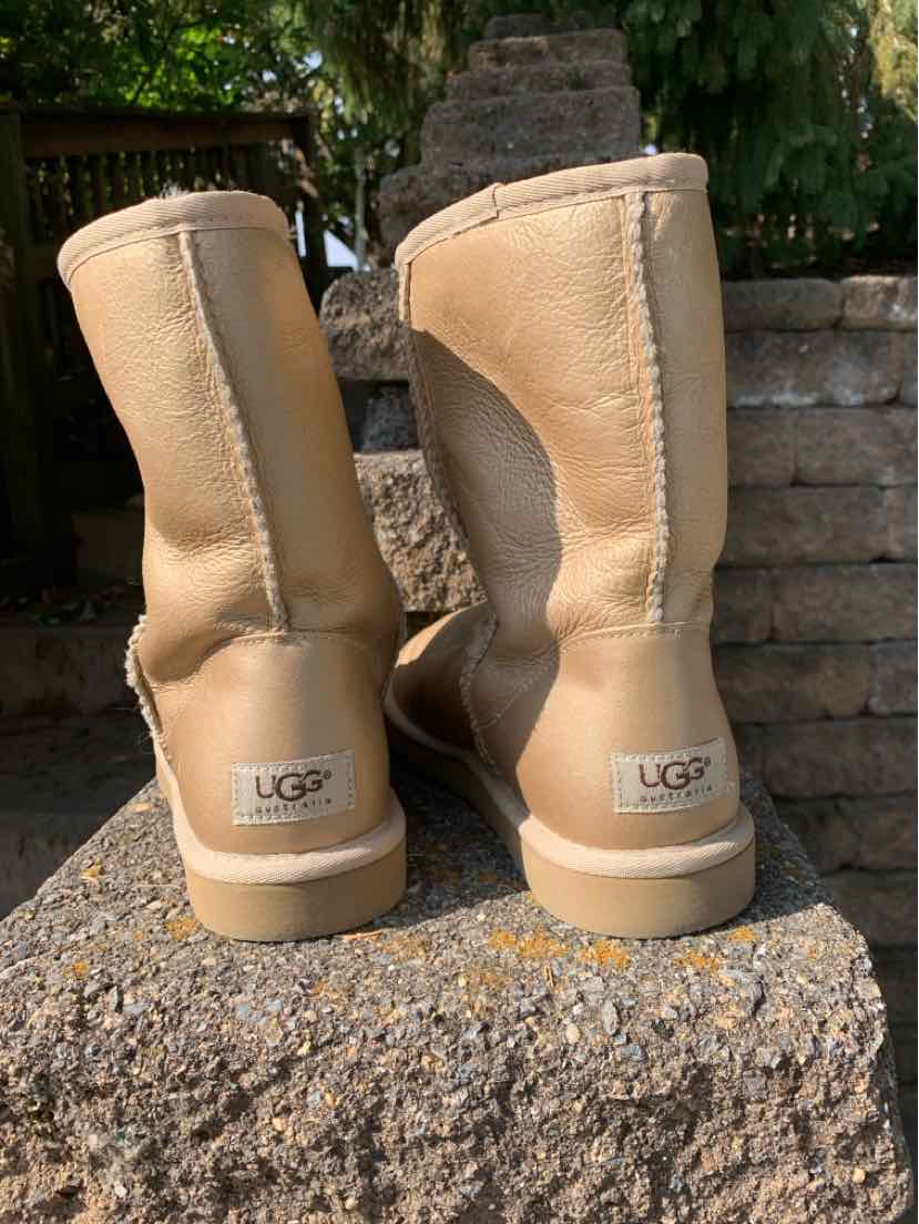 Pair of tan suede UGG boots with rounded toes, rear seams, and logo patches above thick rubber soles.