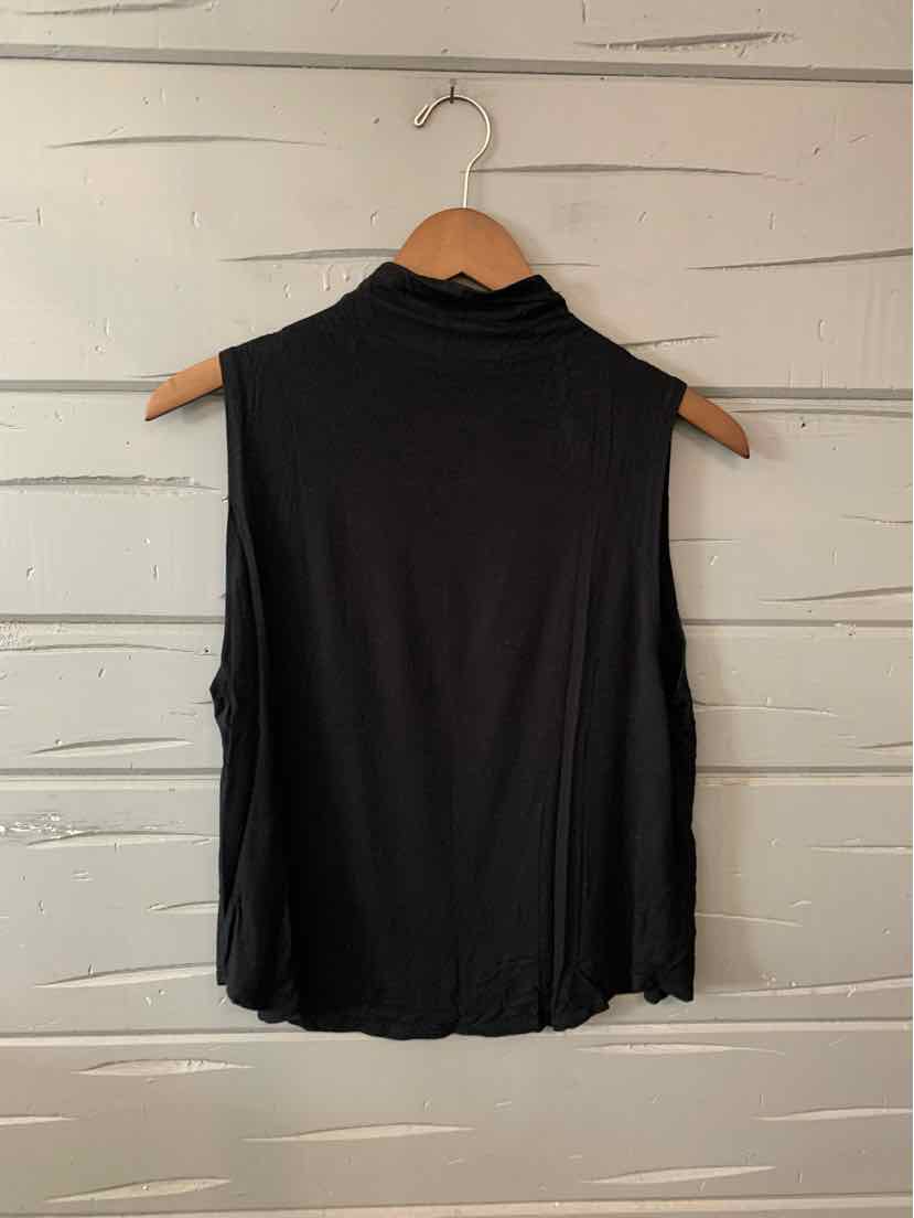 Sleeveless black top with high neckline and relaxed fit on wooden hanger against white paneled wall.