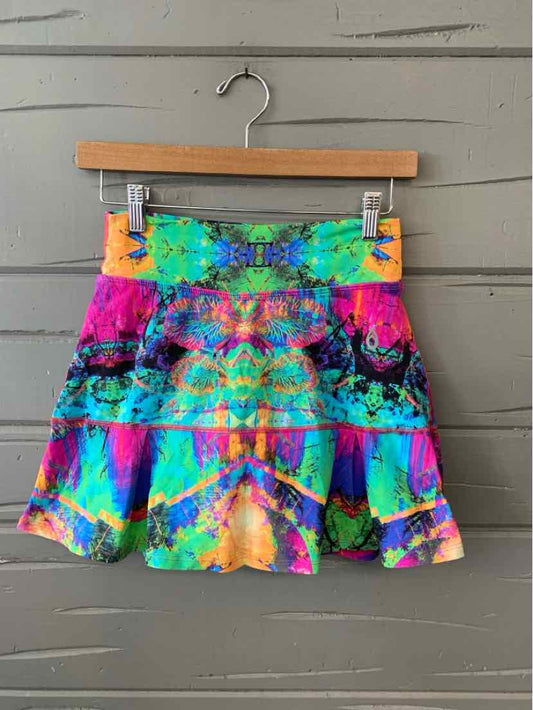 Colorful tie-dye mini skirt with ruffled hem and orange waistband detail hanging on wooden hanger.