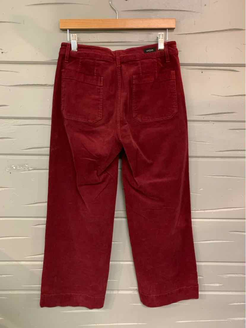 Deep burgundy corduroy pants with a straight leg cut and rear patch pockets hanging on a wooden hanger.