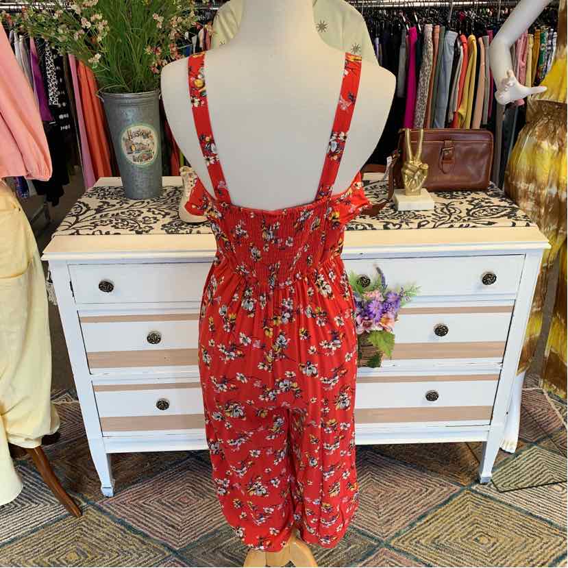 Red floral sleeveless jumpsuit with adjustable straps and smocked back waist, mid-length pants.