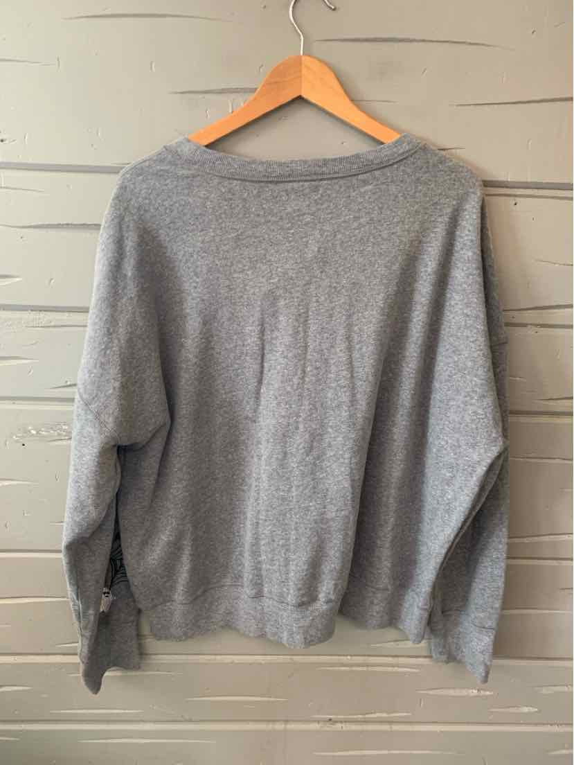Gray long-sleeve knit sweater with a loose fit, displayed on wooden hanger against a pale wood wall.