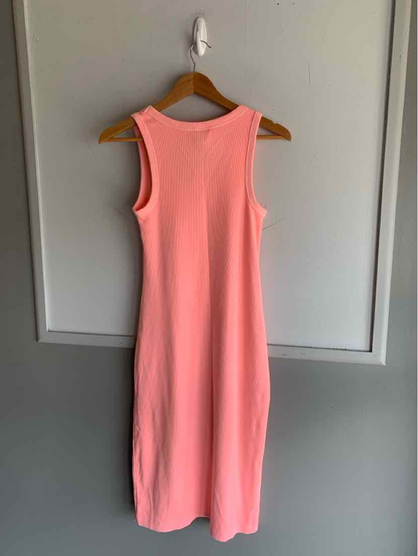 Sleeveless coral pink midi dress with a fitted silhouette hanging on wooden hanger against gray wall.