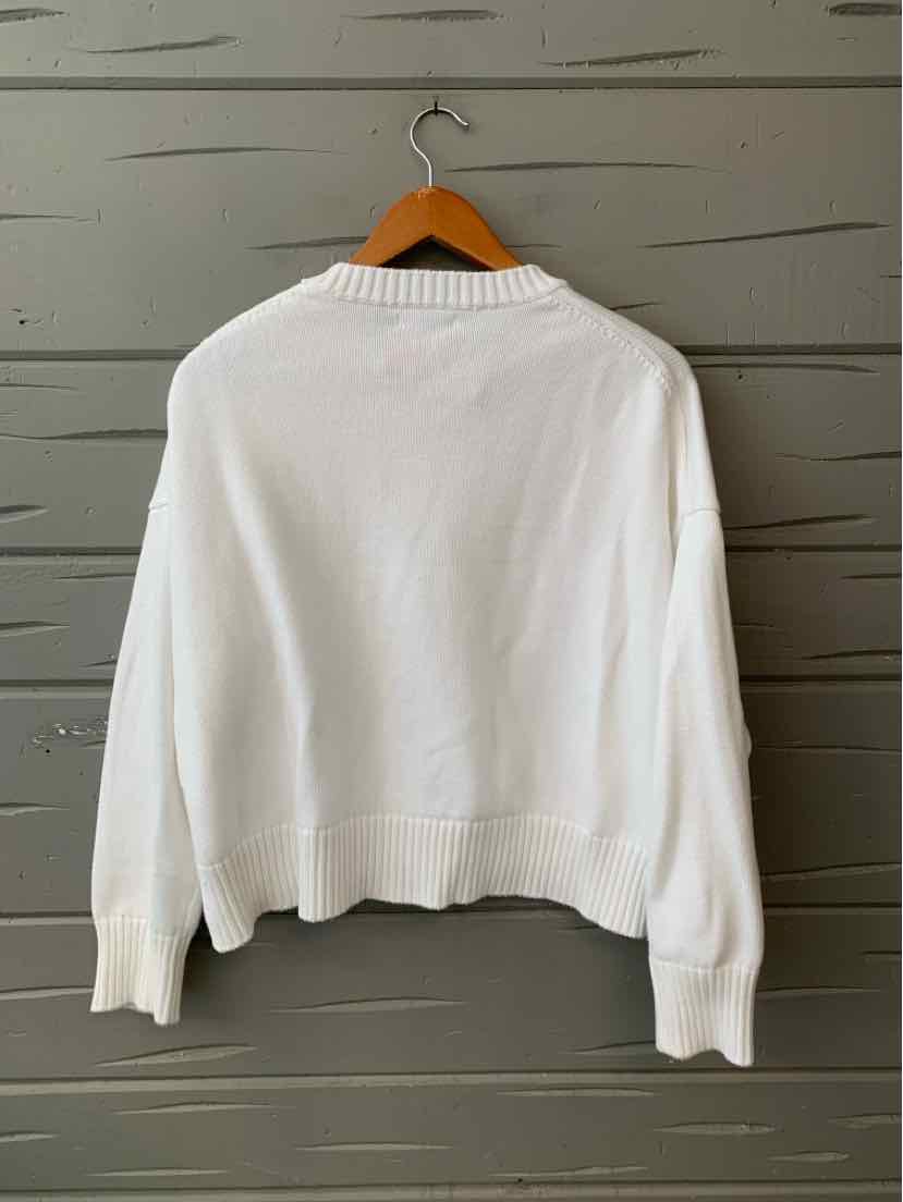 White knit sweater with ribbed cuffs and hem, relaxed fit, hanging on wooden hanger.