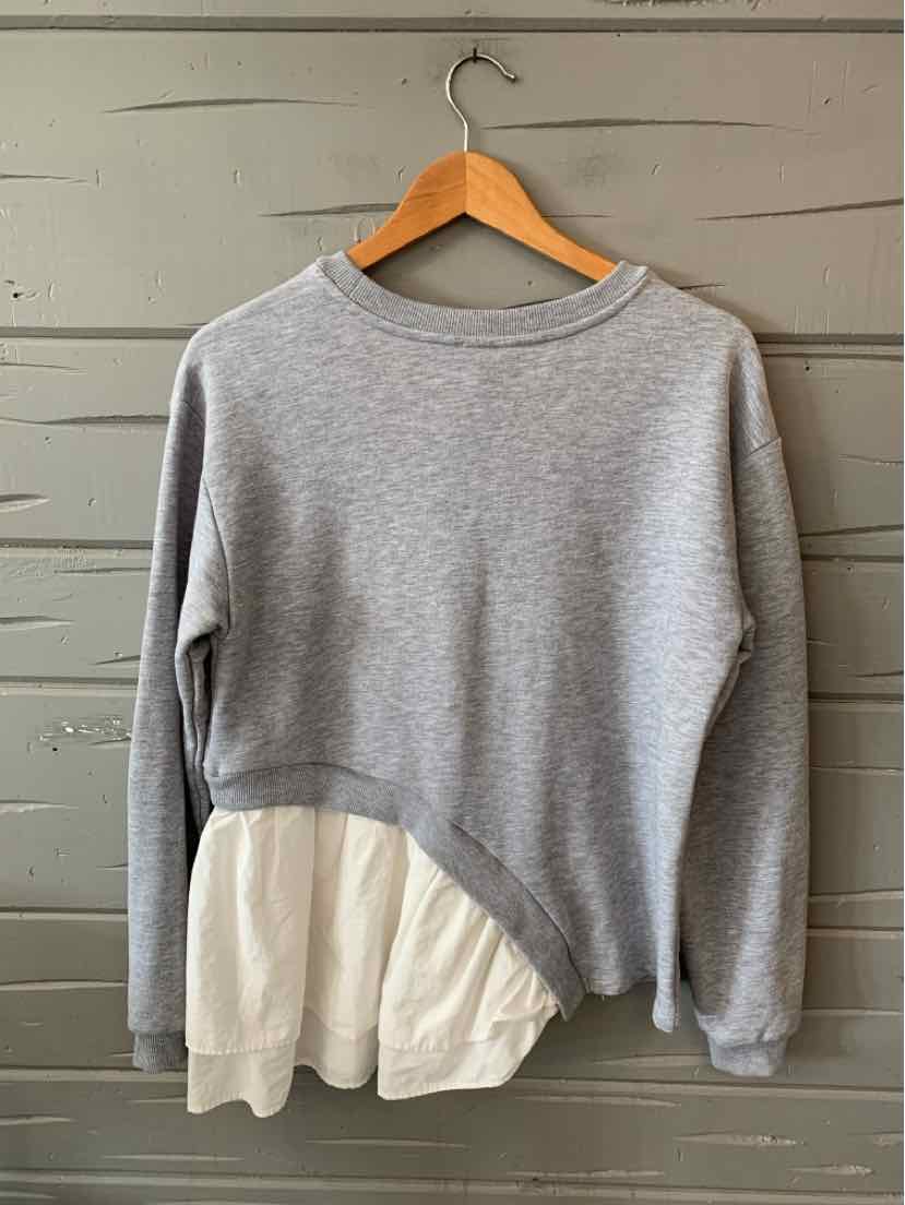 Gray long-sleeve sweatshirt with round neckline and asymmetrical hem featuring white layered fabric detail.