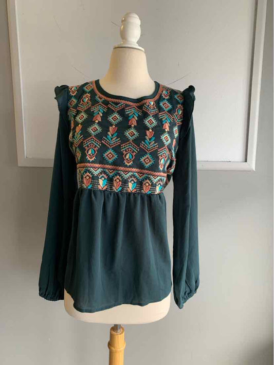 Teal long-sleeve blouse with embroidered geometric pattern and ruffled shoulder detailing.