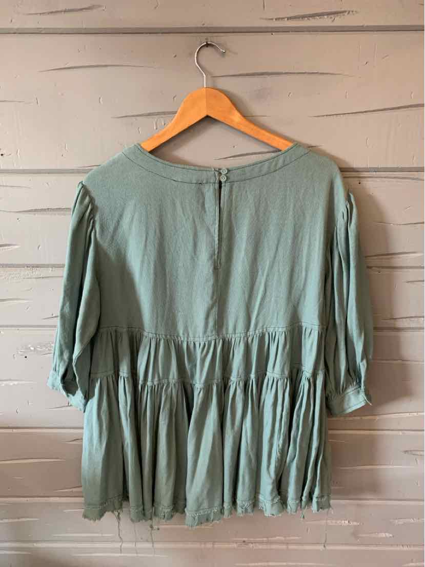 Sage green loose-fit blouse with gathered waist and three-quarter sleeves on a wooden hanger.