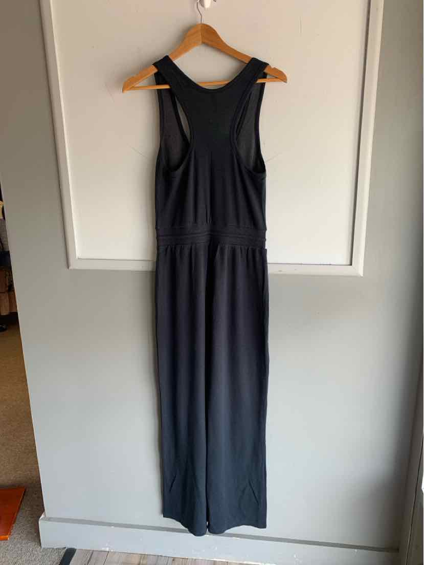 Sleeveless dark gray jumpsuit with scoop neckline and gathered waist hanging on wooden hanger.