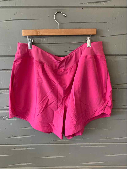 Bright pink athletic shorts with a smooth waistband and relaxed fit hanging on wooden hanger against gray wooden background.
