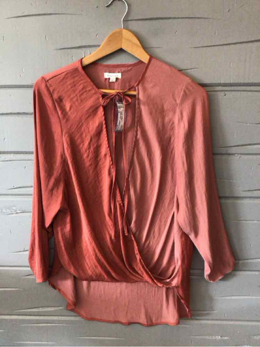 Rust-colored long-sleeve wrap blouse with front tie detail and slightly sheer fabric.