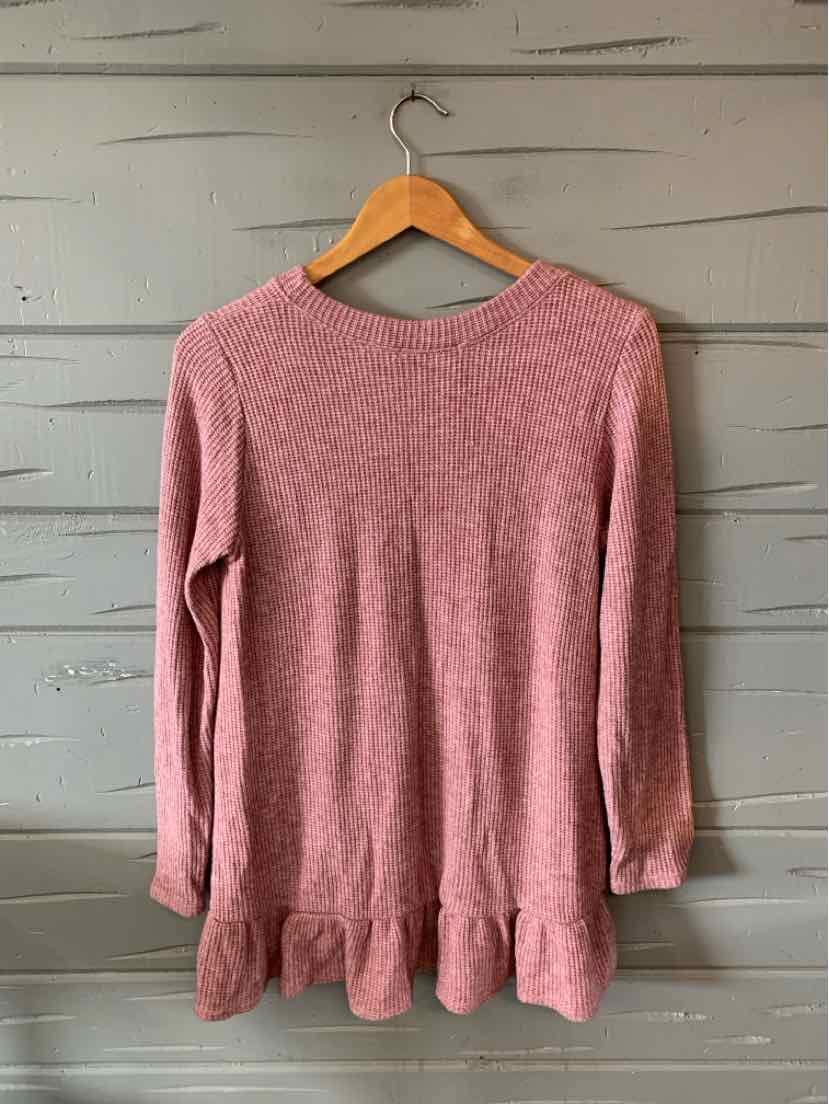 Long-sleeve pink waffle-knit top with ruffled hem and crew neckline hanging on wooden hanger.