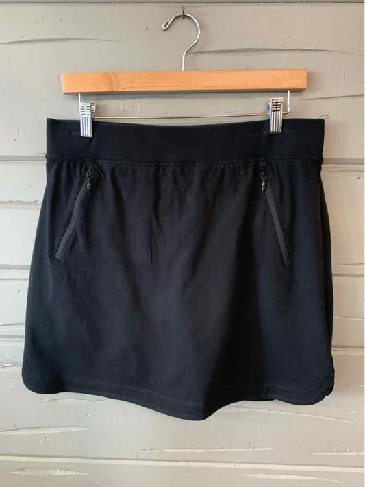 Black knee-length skirt with elastic waistband and front zip pockets hanging on wooden hanger against gray wall.
