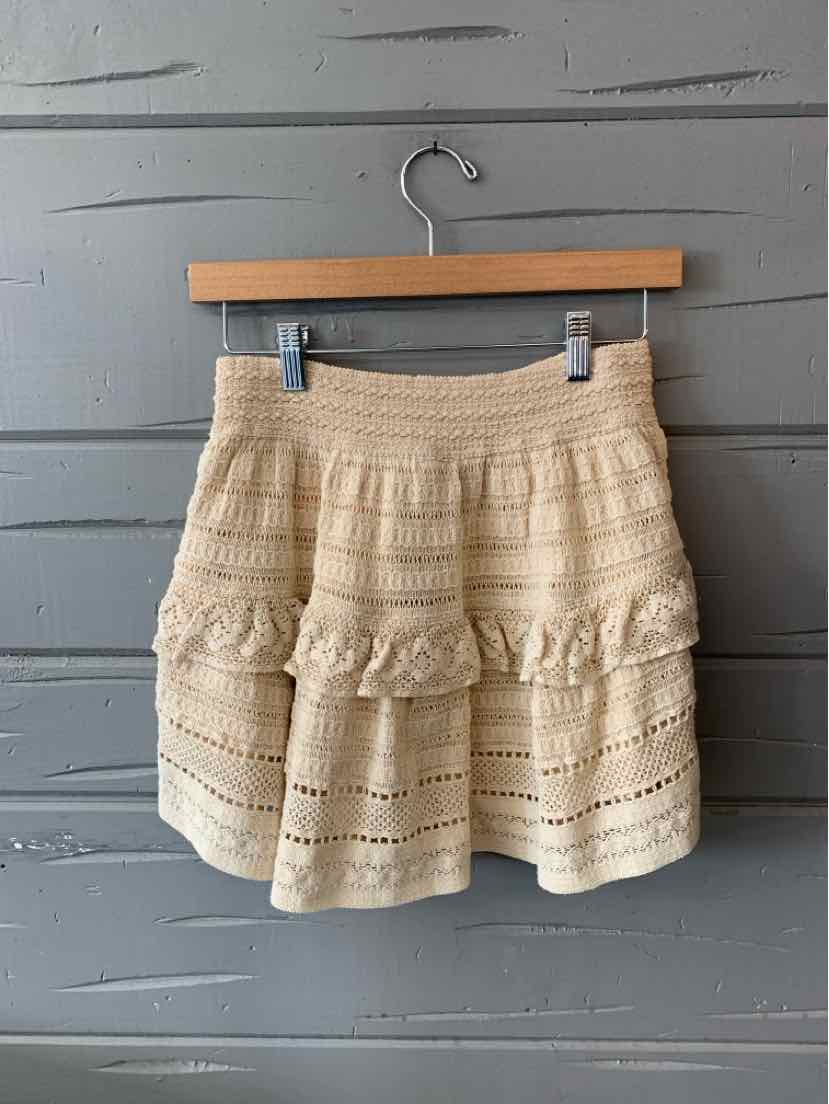 Beige knitted mini skirt with ruffled tiers and a textured lace pattern.