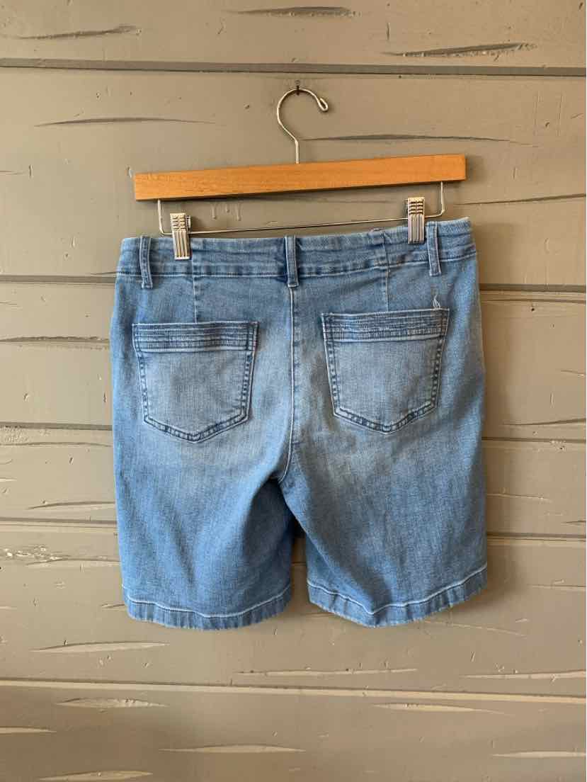 Light blue denim shorts with back pockets and cuffed hems hanging on a wooden hanger against a gray wall.