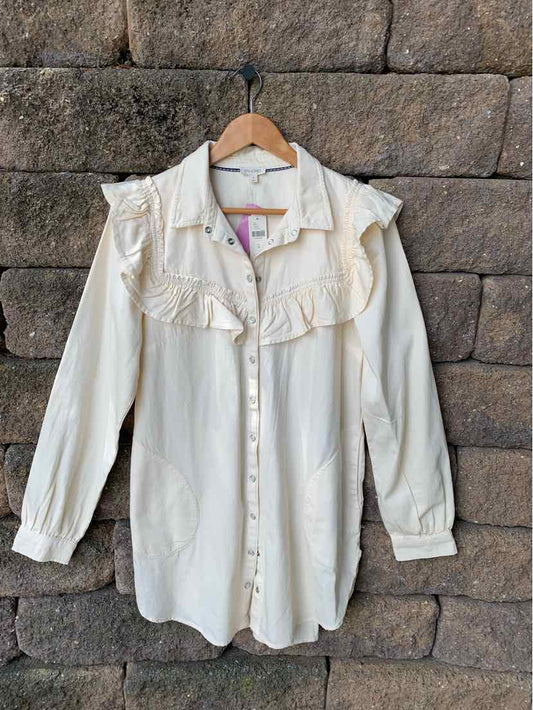 Cream-colored long-sleeve blouse with ruffled yoke and button-down front on wooden hanger.