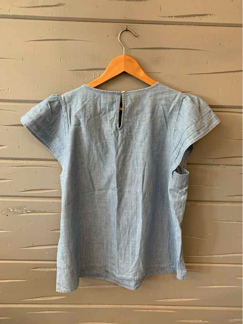 Light blue chambray short-sleeve blouse with a loose fit and round neckline, hanging on wooden hanger.