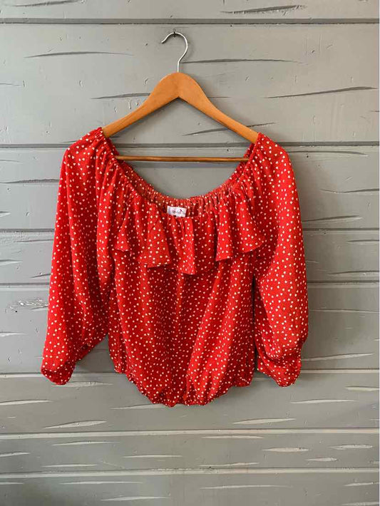 Red long-sleeve blouse with white heart print and ruffled neckline on wooden hanger.