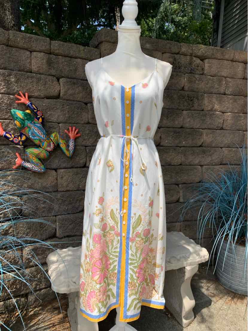 White midi dress with pink floral print, yellow and blue vertical stripes, sleeveless with a cinched waist.